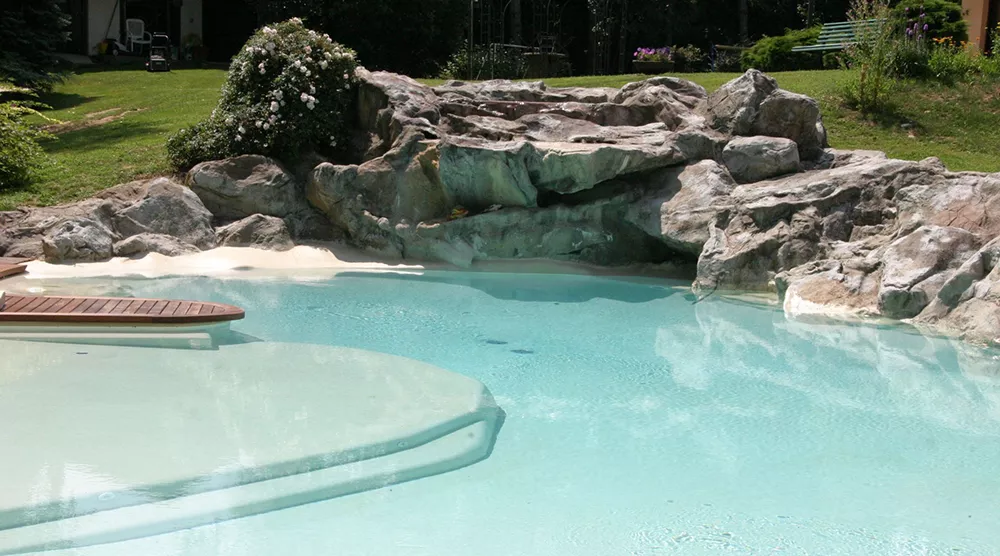 Piscina effetto spiaggia con pontile in legno e rocce - Baires Piscine